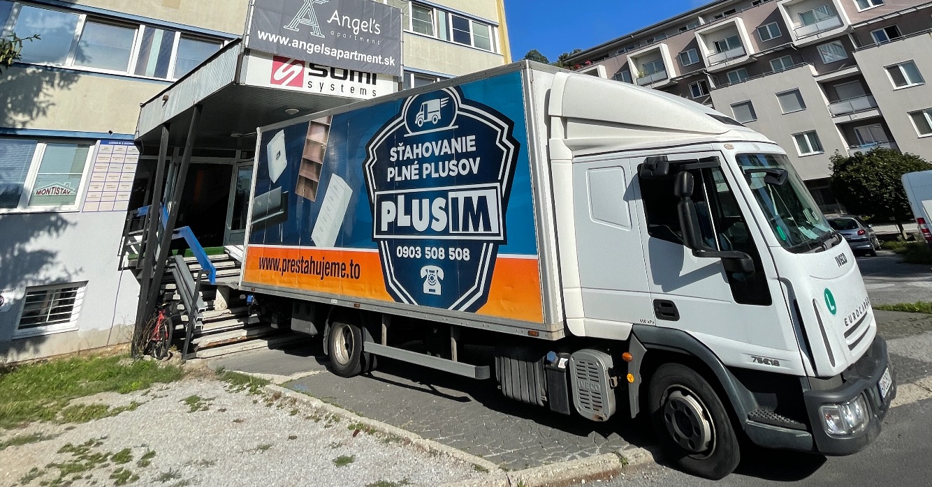 Sťahovacie vozidlo PLUSIM zaparkované pred administratívnou budovou počas realizácie sťahovania za slnečného dňa